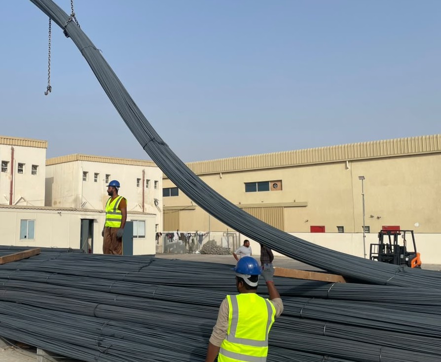 Workers handling bundles of reinforcing steel at a yard